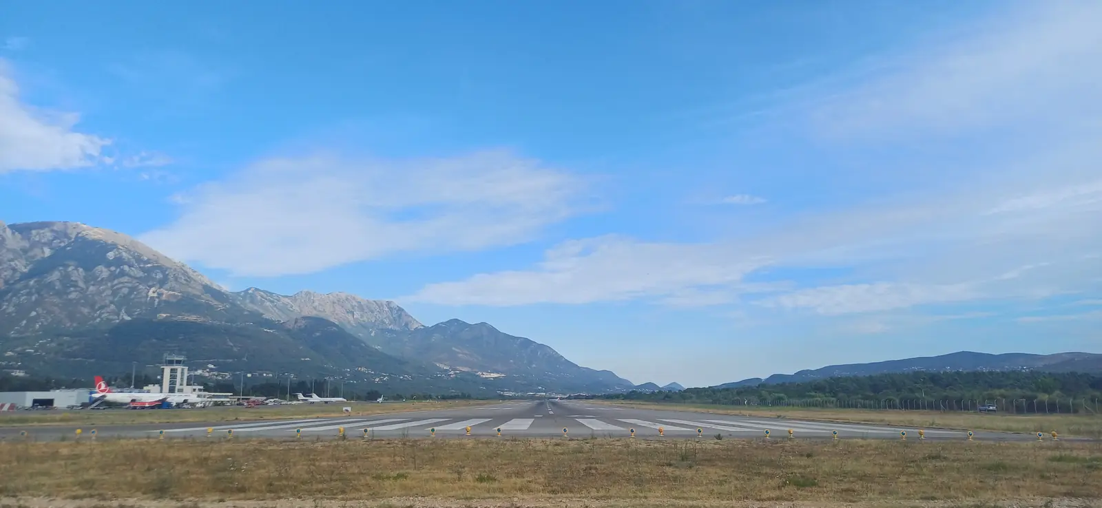 Dráha letiště Tivat, vlevo terminál a věž, v pozadí hory nad Bokou kotorskou