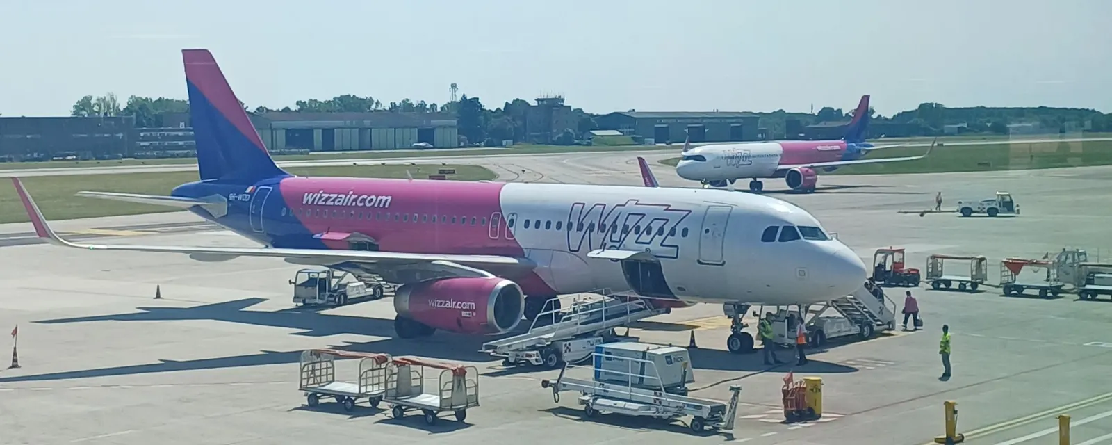Airbus Wizz Air u stání na letišti Treviso, kolem vozíky na zavazadla, v pozadí další Wizz Air