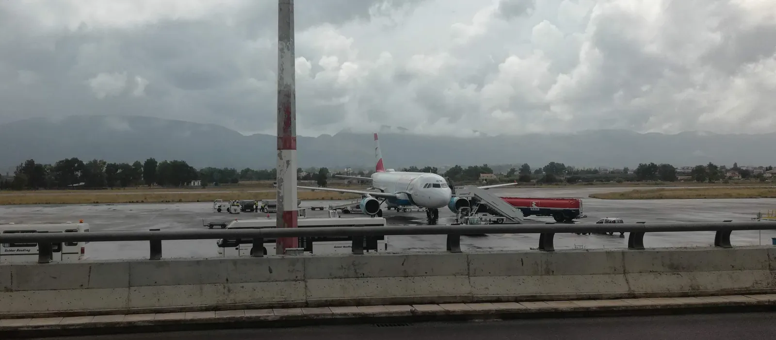 Airbus v barvách Austrian Airlines na mokré odbavovací ploše letiště Zakynthos pod mraky